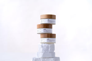Stack of Minerva Sol, Aura and Luna body butter jars on a white plinth
