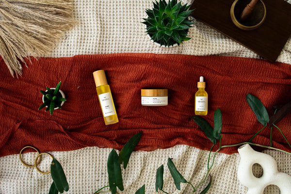 Minerva Aura body oil, body butter and scalp oil laid on a rust linen cloth