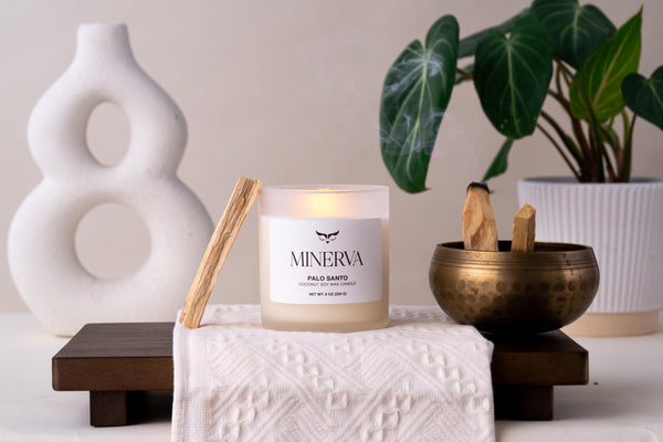 Lit Minerva Palo Santo candle on a wooden tray with a brass bowl and palo santo stick