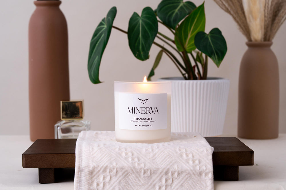 Lit Minerva Tranquility lavender candle on a wooden tray beside a plant and vase