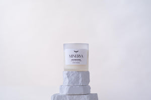 Minerva Unconditional 8 oz frosted glass candle on a white stone plinth