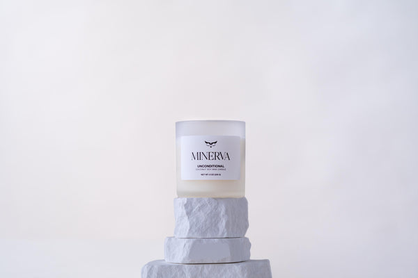 Minerva Unconditional 8 oz frosted glass candle on a white stone plinth