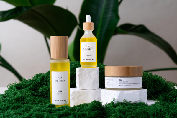 Minerva body oil, scalp oil and body butter trio on green moss with tropical leaves