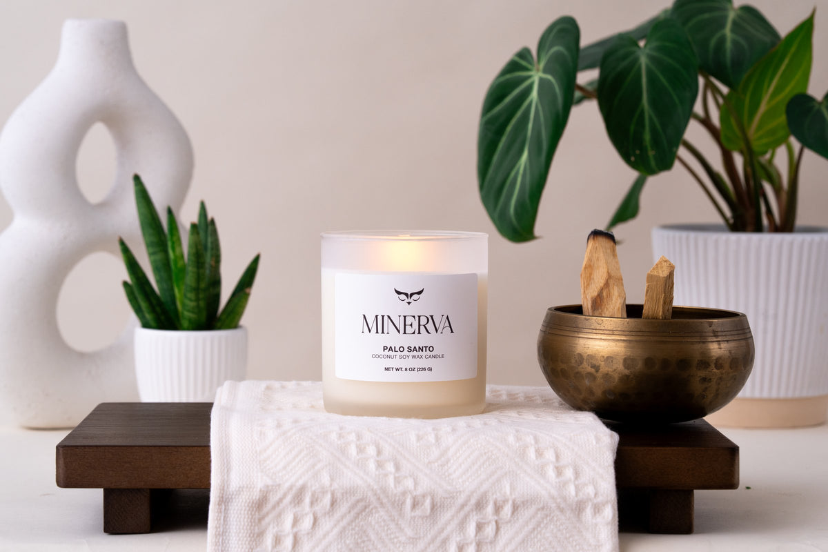 Lit Minerva Palo Santo candle on a wooden tray with stacked books and plants