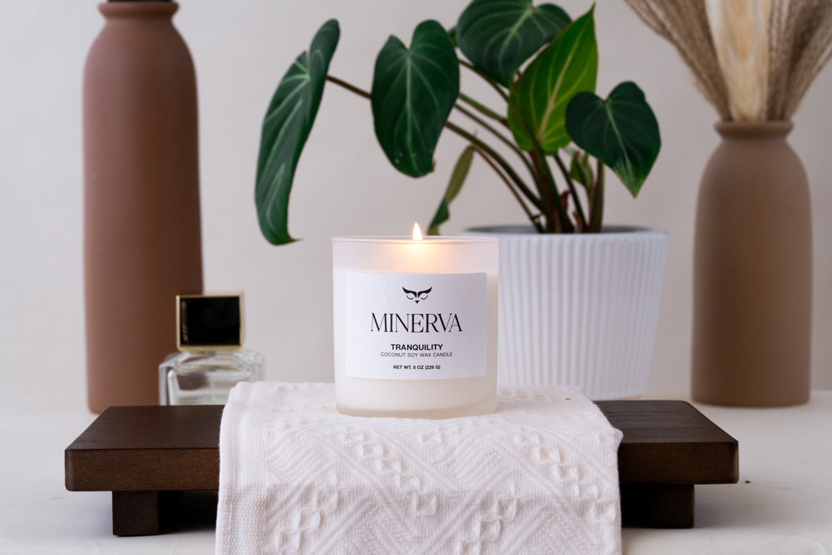 Lit Minerva Tranquility candle on a wooden tray beside a plant